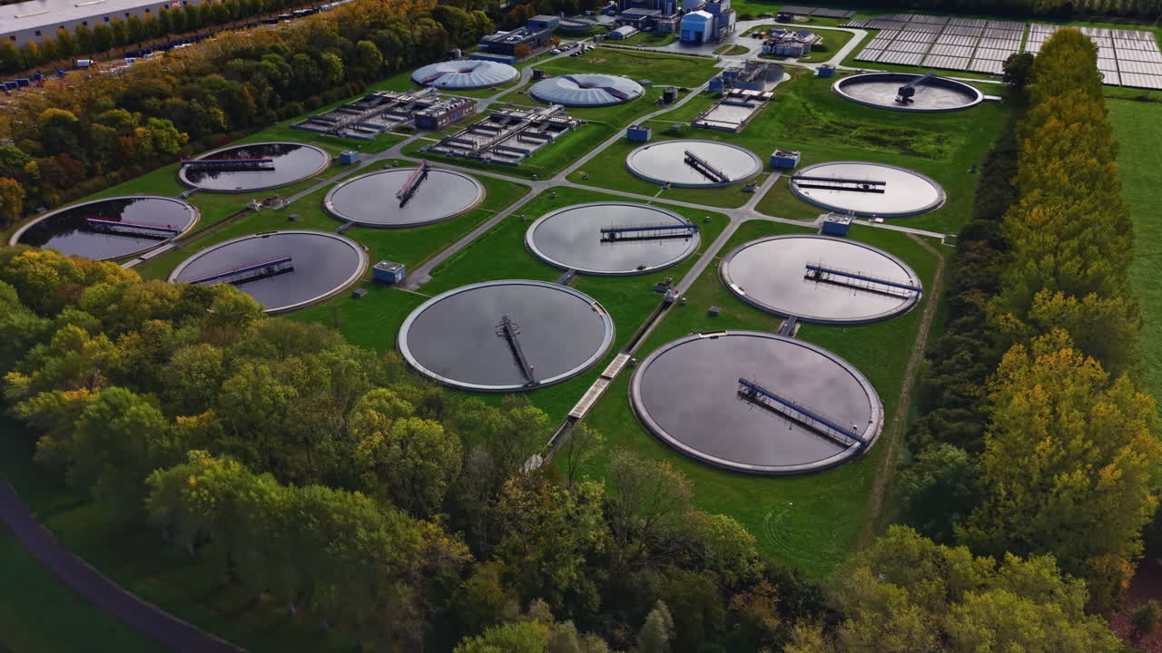 Large wastewater treatment facility surrounded by green trees under clear blue sky during midday hours