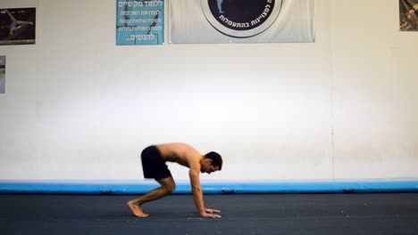 una foto fija de un tipo musculoso sin camisa haciendo el pino en el gimnasio de gimnasia