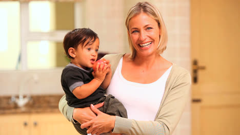 Young-mother-posing-with-her-baby-eating-an-apple-on-her-hip