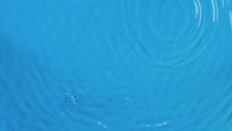 raindrops fall on waves in blue water. top view. drop falls into the water