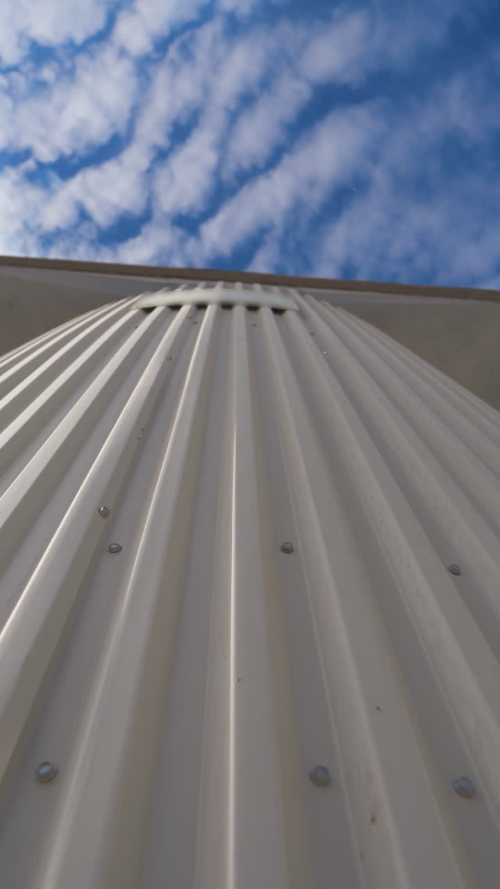 Metal construction on the modern factory. Storage tanks for processing grains on sky background. Smoke releasing from industry into the air. Close-up. Motion camera top down. Vertical video