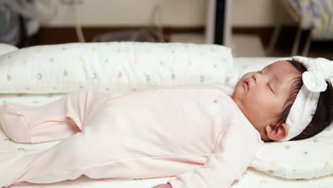 peacefully sleeping as her head is laid on a pillow, a newborn child is in deep slumber on a mattress inside a nursery room