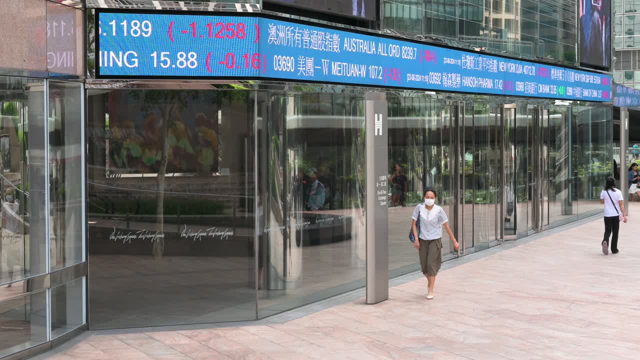 People walk through the financial district of Hong Kong, passing a moving screen at Exchange Square that shows negative stock ticker symbols, home to the Hong Kong Stock Exchange (HKEX).