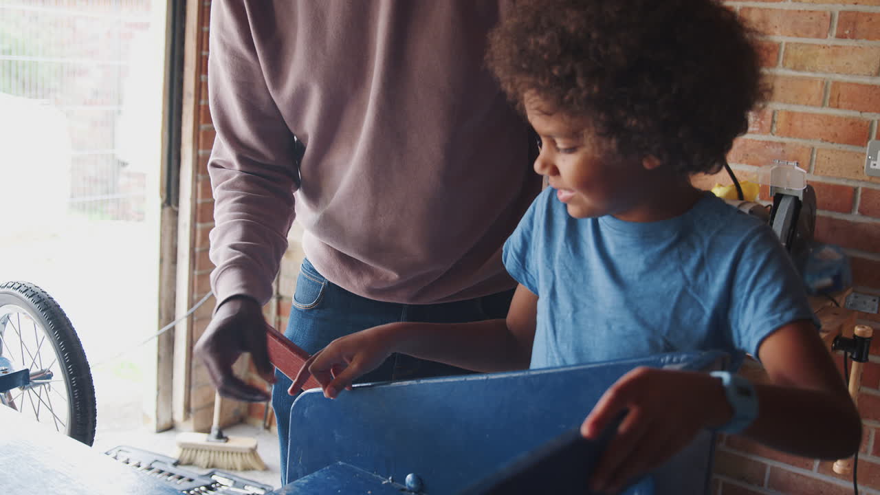 pre adolescente de raza mixta de pie en un banco de trabajo haciendo un kart de carreras con su padre en su garaje, de cerca, cintura hacia arriba