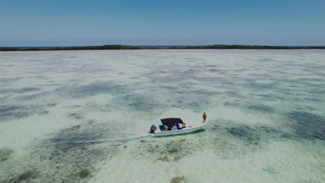 a small fishing boat with a guide at the bow in the clear waters of los roques, aerial view