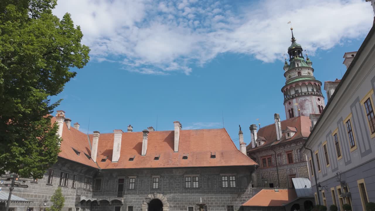 Historic Český Krumlov Castle courtyard on a sunny day with blue skies and lush trees
