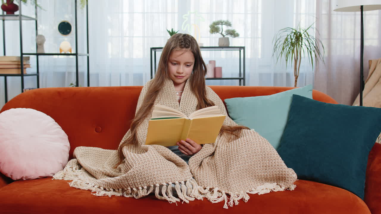 Ragazza avvolta in una coperta che si rilassa leggendo un libro, sfogliando le pagine, sorridendo e godendosi la letteratura