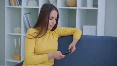 mujer escribe mensajes usando el teléfono móvil sentada en el sofá en la sala de estar