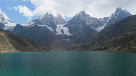 stunning aerial tilt-up shot reveals a vast turquoise glacial lake, rising to the dramatic, snow-covered peaks of the cordillera huayhuash on peru’s legendary trekking route