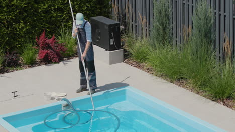 a worker cleans a swimming pool with a special vacuum cleaner. tilt shot