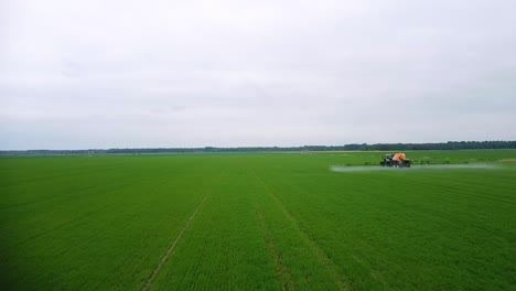 aerial view of tractor spraying pesticide and fertilizer on the green field in overcast summer day, wide angle low altitude drone shot mowing forward