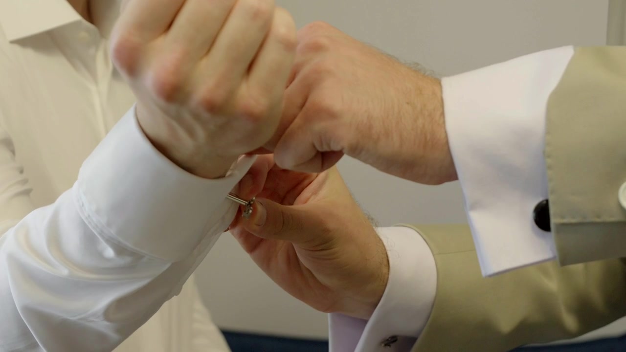 Best man helping the groom fasten his shirt cuff during wedding preparations. A natural moment of friendship before the ceremony