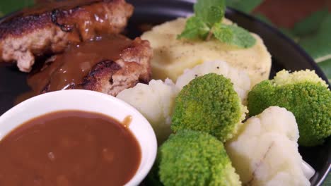 a delicious meal served on a plate with burger patties and vegetables with brown gravy sauce