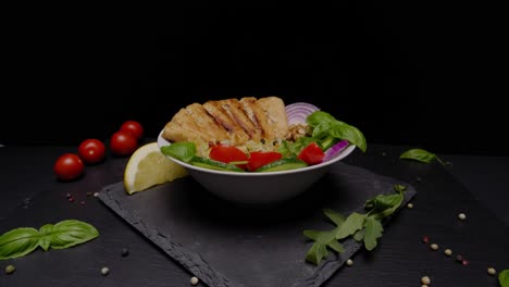 cierre de retroceso de un plato de carne vegana dorada en un tazón de arroz y productos frescos sentados en un plato de pizarra y una mesa, cortado con espacio para copiar