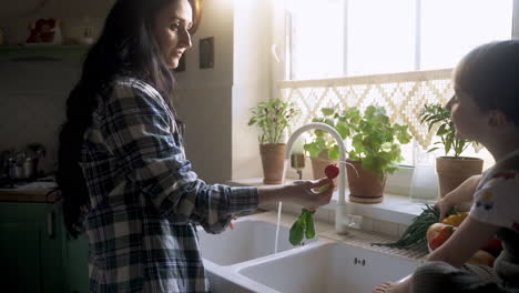 Caucasian-woman-washing-vegetables-and-fruits-in-the-sink.-Her-son-helps-to-her