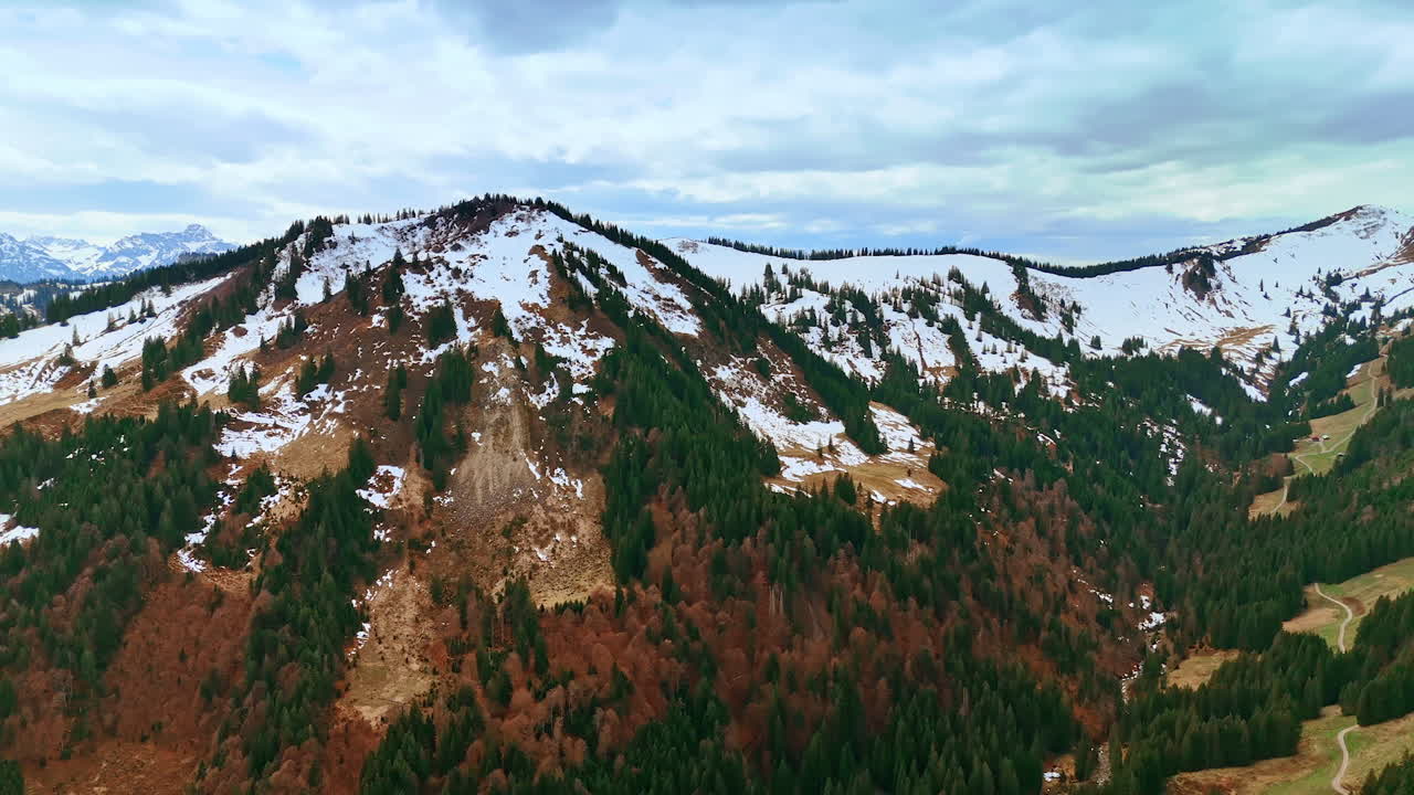 Snow-capped mountains with some green and dry pine trees on the slopes. Drone footage over the wilderness in Germany, Bavaria.