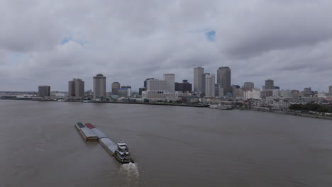 slow panning aerial video of a large barge that is sailing up the mississippi river with downtown new orleans in the background