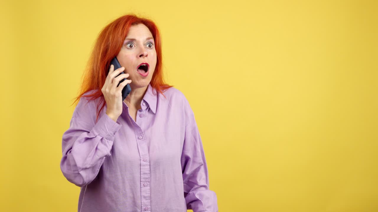 Donna sorpresa con i capelli rossi che parla al telefono con un'espressione scioccata su sfondo giallo