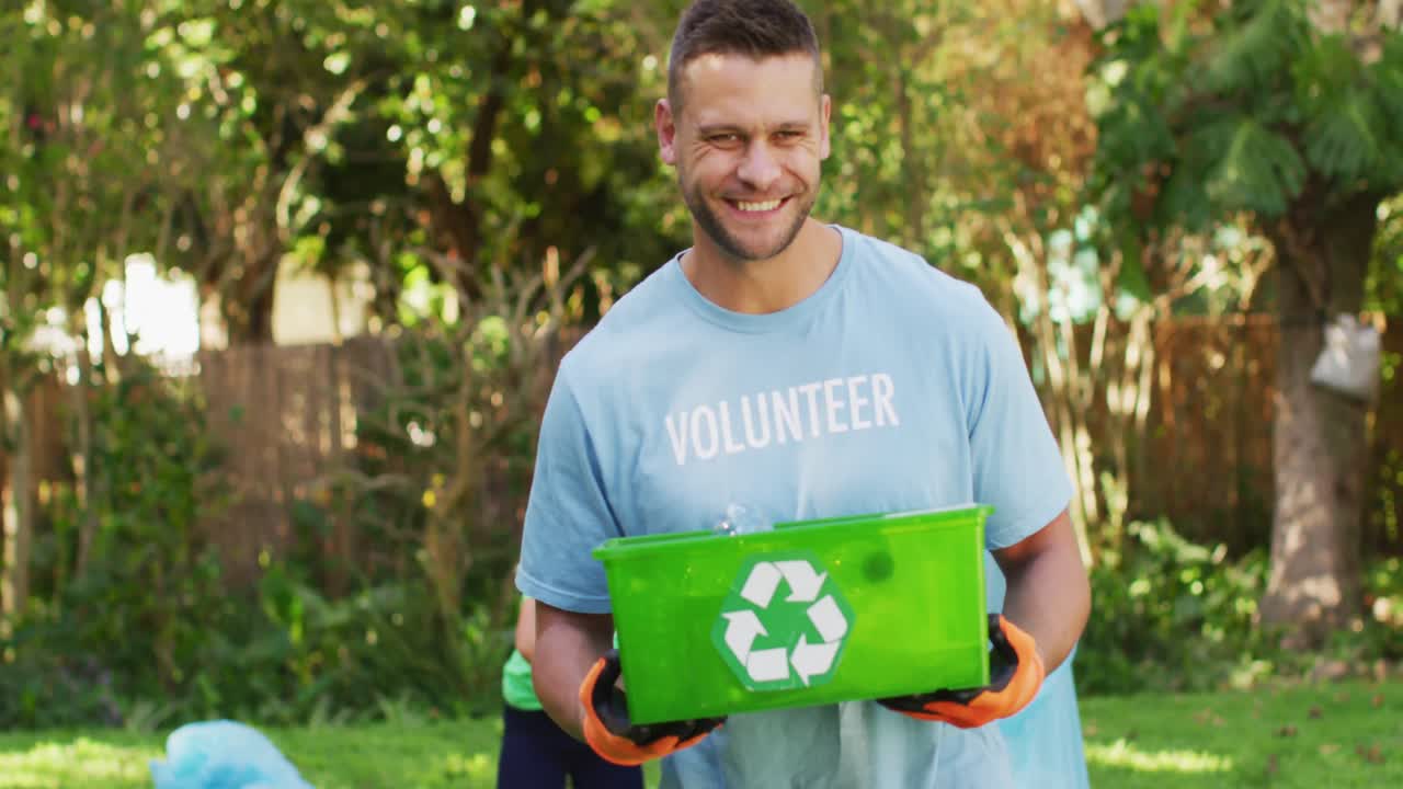 hombre caucásico sonriente con camiseta de voluntario sosteniendo una caja de reciclaje, recolectando residuos plásticos