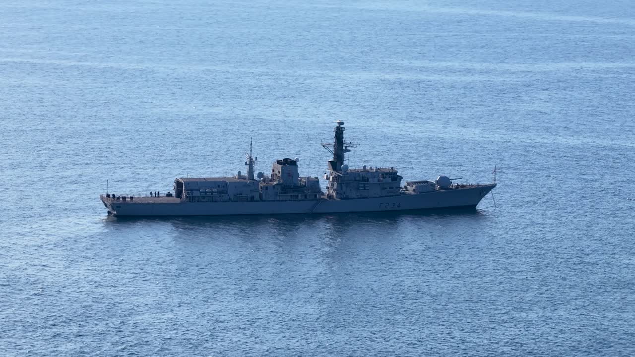 Military vessel moves steadily across tranquil sea under daylight, wide shot, stable camera, clear weather