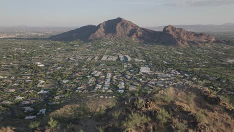 Drone-capturing-luxury-town-of-Paradise-Valley-while-flying-over-Mummy-Mountain-and-revealing-Camelback-mountain-at-background-in-Arizona,-USA