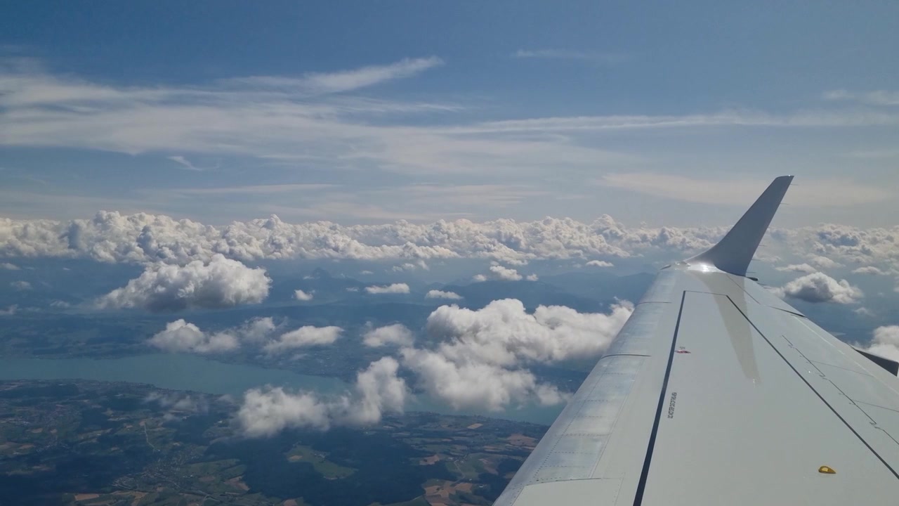 Vista dal finestrino di un aereo sul Lago di Costanza, con l'ala del velivolo sopra soffici nuvole bianche, creando una scena di cielo sereno associata al viaggio aereo, alla libertà, alla tranquillità e all'avventura