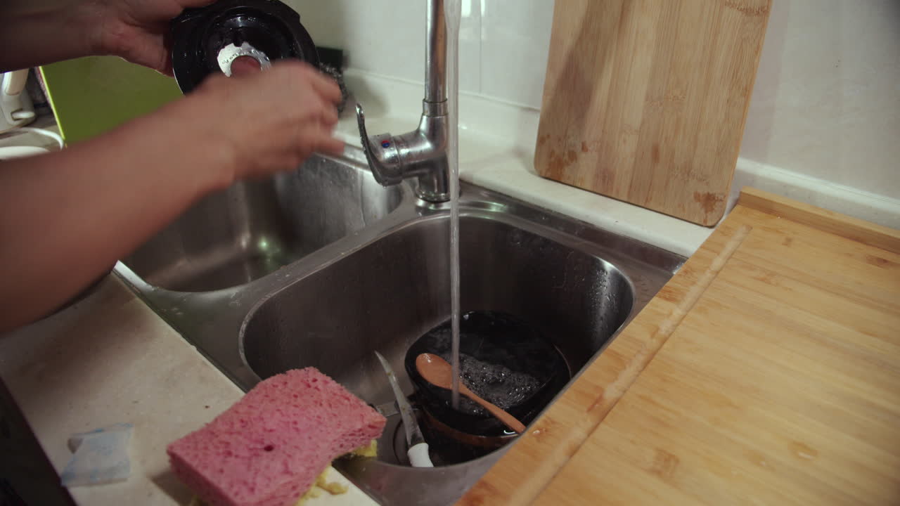 Kvinde vasker blender i en vask under vandhanen.