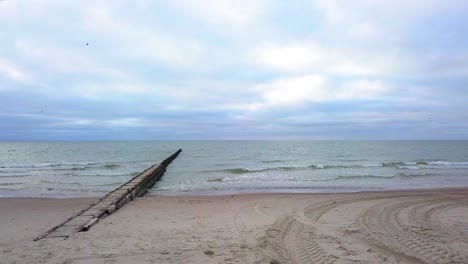 establishing aerial view of baltic sea coast on a overcast day, old wooden pier, white sand beach, low waves crushing against the coast, climate changes, low wide angle drone shot moving forward