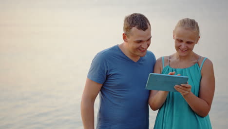 una pareja joven usando una tableta junto al mar.