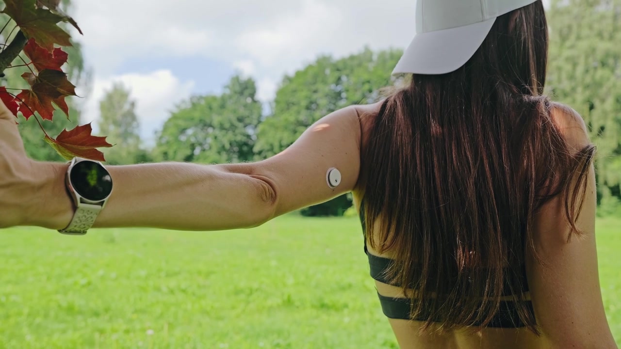 Donna con sensore di glucosio che esegue uno stretching della parete toracica al parco, vivendo con il diabete