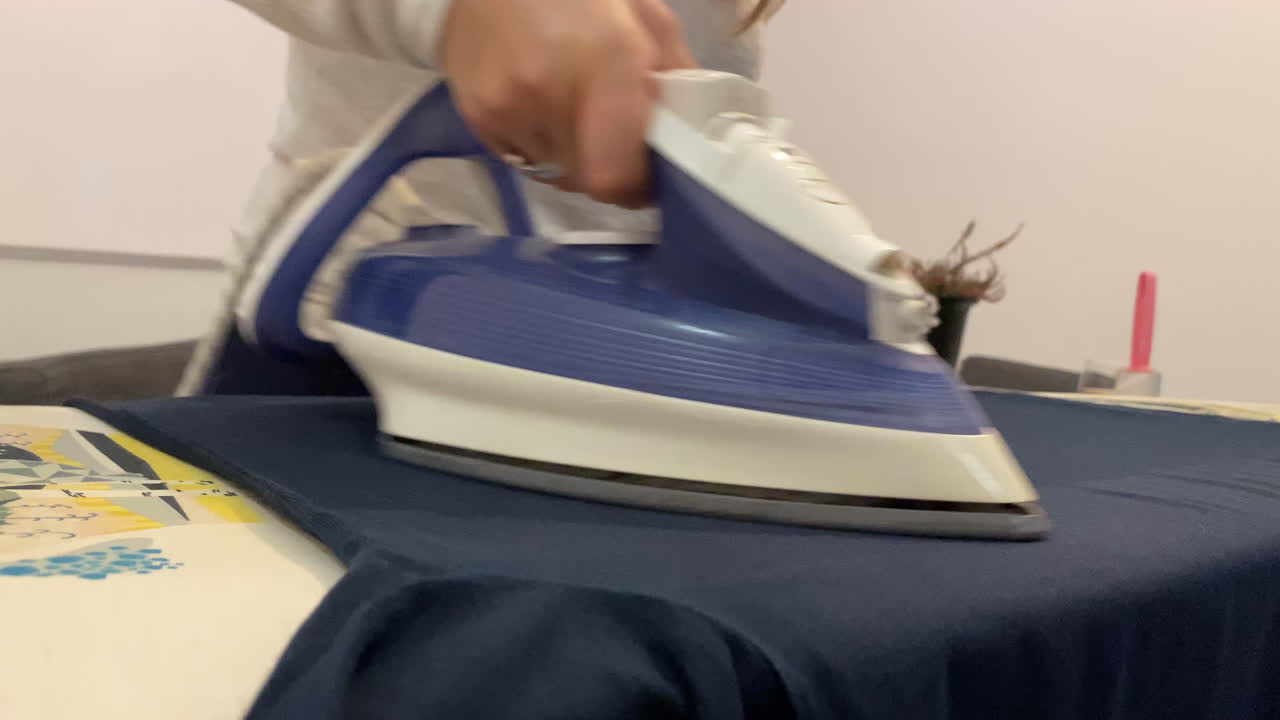 The girl unfolds her shirt on the ironing board and starts ironing