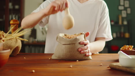 person scooping beans into a burlap sack in a kitchen