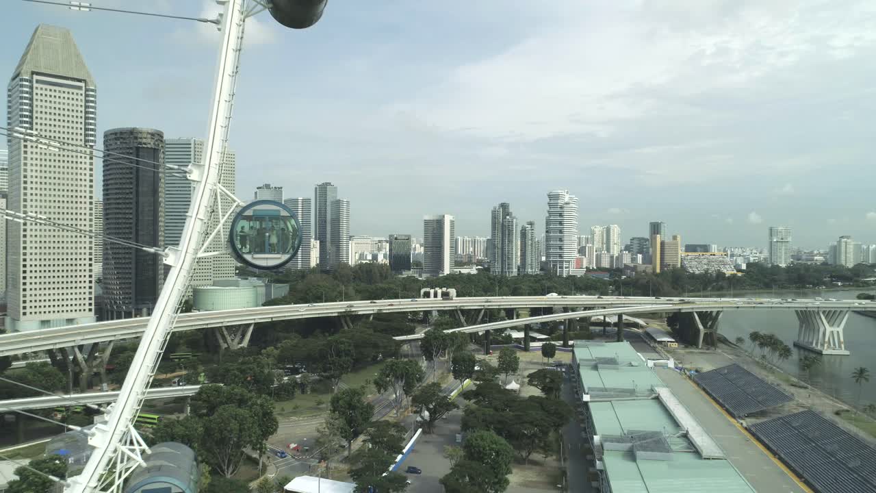 volando cerca de una gran noria gigantesca con gente dentro, mostrando el horizonte de la gran ciudad de singapur con tráfico de automóviles, puentes, torres de rascacielos