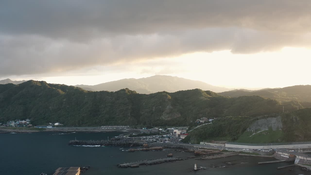 4K Drone footage showing a still aerial view of mountains during sunset with the shoreline and calm sea in the distance. The soft light creates a peaceful natural atmosphere. For travel films