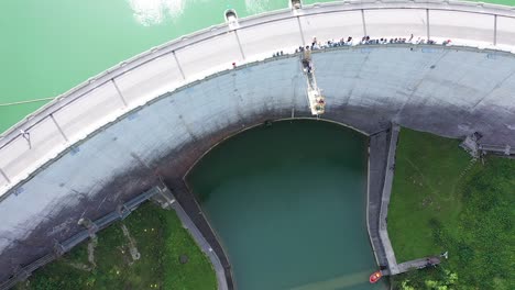 Aerial-birds-eye-top-down-drone-view-of-50m-high-bungee-jumping-dam-platform,-viewers-standing-on-dam-bridge-watching-action-happen