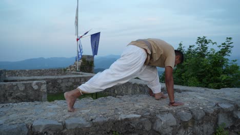 hombres asiáticos haciendo una postura de hatha yoga al amanecer en la parte superior de la pared de piedra