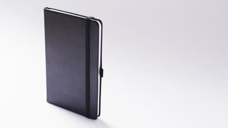 Closed-black-notebook-standing-vertical-with-copy-space-on-white-background-in-slow-motion