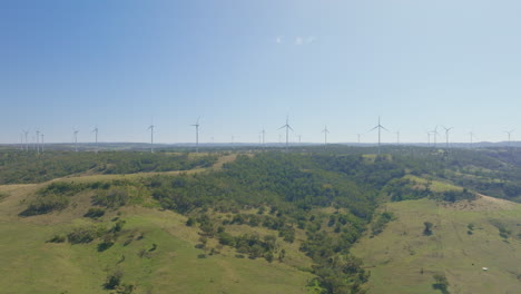 long row of wind turbines on green hill in distance, 4k drone flyover