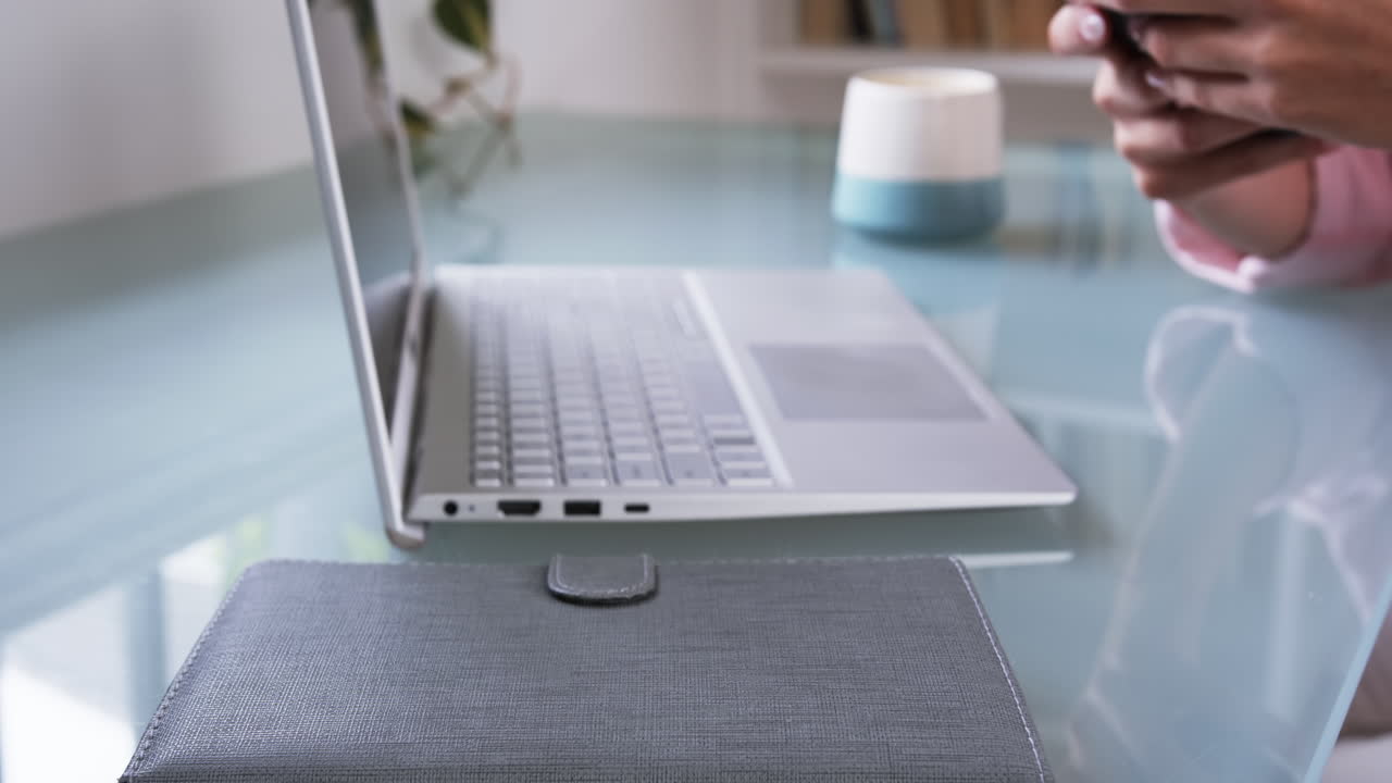Working from home, woman using smartphone near laptop on glass desk