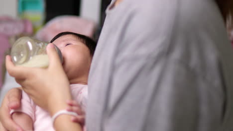 holding a baby bottle in one hand and cradling the sleeping newborn child in her other arm as the mother is giving some milk to her child