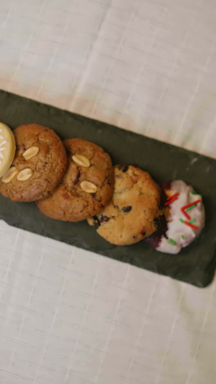 Variety of Christmas cookies on a rotating dark chalkboard, decorated with icing, sprinkles and festive figures in the foreground