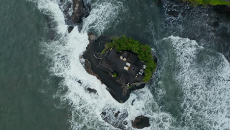 Vista-Aérea-Aérea-Del-Templo-De-Tanah-Lot-En-Un-Pequeño-Acantilado-Rocoso.-De-Arriba-Hacia-Abajo,-Incline-Hacia-La-Plataforma-Rodante-Del-Famoso-Templo-Hindú-En-Una-Pequeña-Isla-Con-Fuertes-Olas-Rompiendo-En-Bali,-Indonesia