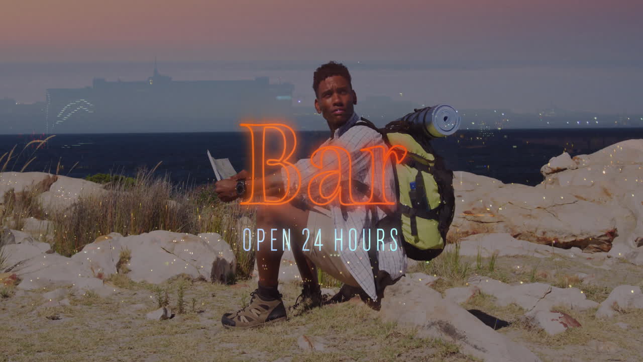 Male hiker squatting on rocky shore, examining map while neon bar sign glowing for travel marketing