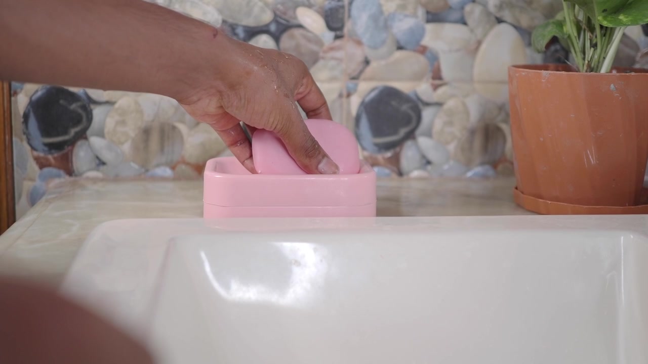 Persona tomando una pastilla de jabón rosa de la jabonera en el lavabo del baño