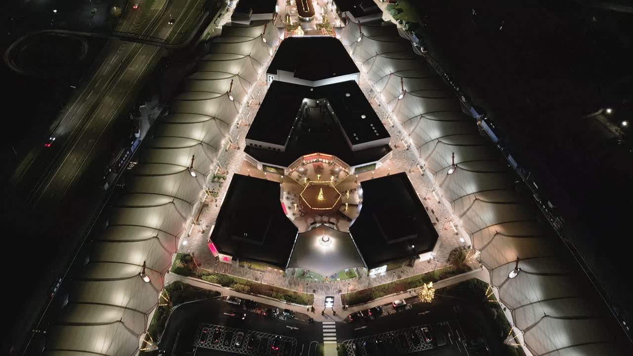 volando sobre mcarthur glen vista aérea iluminada por la noche de la salida y estacionamiento de diseñadores de lujo, ashford, kent