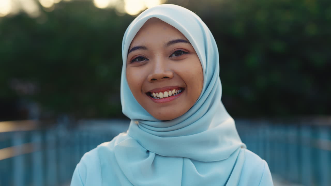 Close-up portrait of a young Muslim woman smiling in a light blue hijab