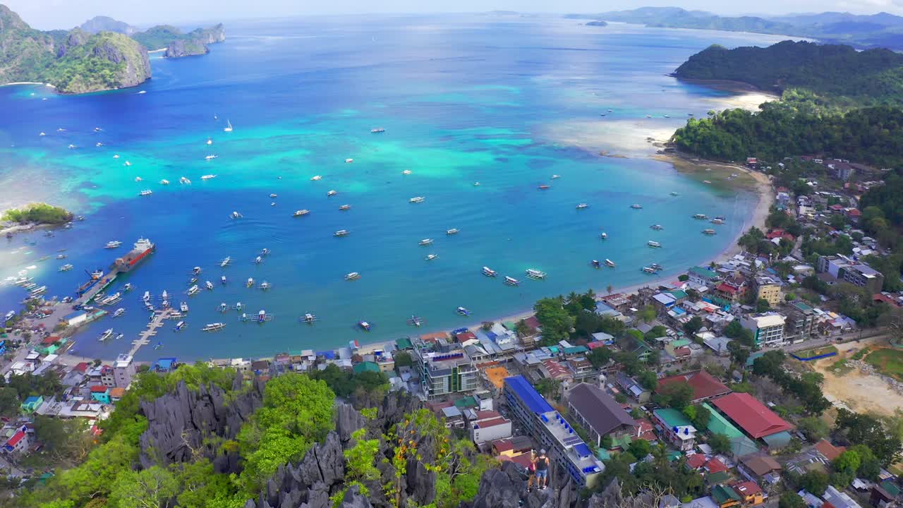 남자와 여자가 필리핀 팔라완의 엘 니도 (el nido) 의 항구와 푸른 바다 호수 (blue sea lagoon) 를 내려다보는 산의 바위 꼭대기에 서 있습니다.