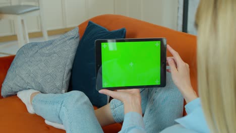 usando gestos con un dispositivo de pantalla táctil, navegando por internet, viendo contenido. mujer en casa descansando en un sofá usando con pantalla de maqueta verde tableta computadora en modo paisaje horizontal.