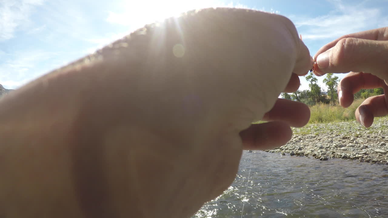 fly fisherman tying on a fly to his line while float fishing on a river in the mountains