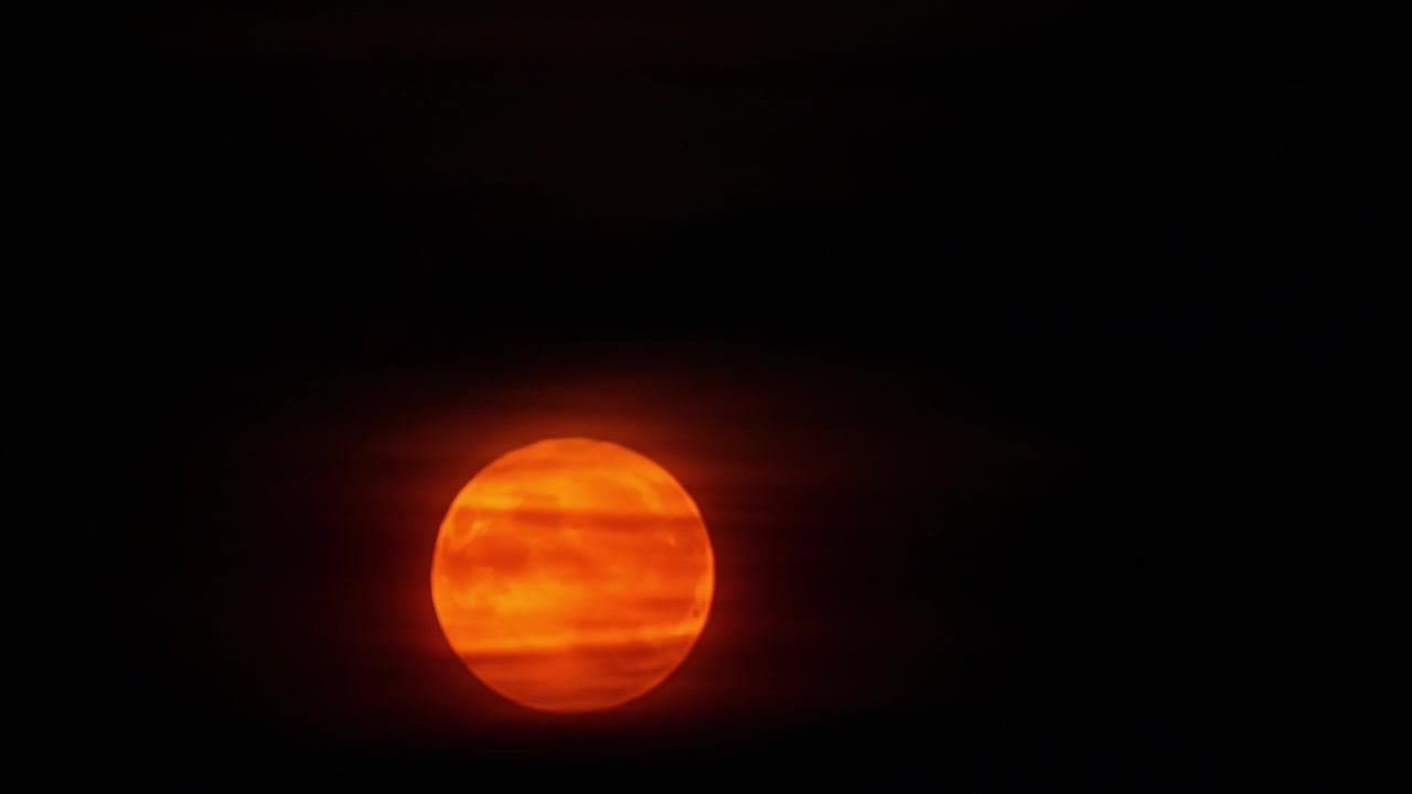 Moon setting beyond clouds illuminating orange glow